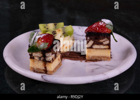 Tiny tortina con kiwi, panna montata e torta al cioccolato su un marmo nero tabella Foto Stock