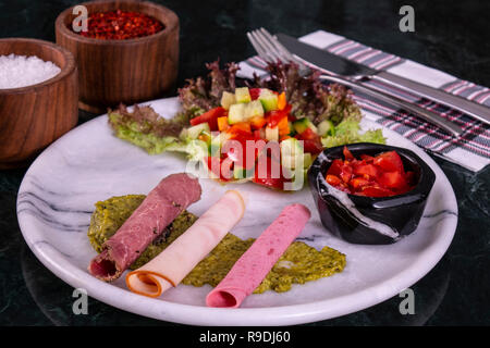 Piastra di carne con fette sottili di salumi e prosciutto con insalata sullo sfondo marmo Foto Stock
