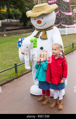 Bournemouth, Regno Unito. Il 23 dicembre 2018. Il pupazzo di neve e visita Snowdog Bournemouth, bella rinfrescata una grigia giornata drizzly come coda di bambini eccitato per avere le loro foto scattata con loro in Giardini inferiori di Bournemouth. Due bambine posano con il pupazzo di neve. La struttura ad albero di Varsavia, parte del Bournemouth albero di Natale il paese delle meraviglie in background. Credito: Carolyn Jenkins/Alamy Live News Foto Stock