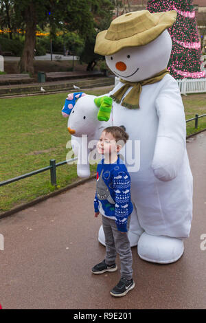 Bournemouth, Regno Unito. Il 23 dicembre 2018. Il pupazzo di neve e visita Snowdog Bournemouth, bella rinfrescata una grigia giornata drizzly come coda di bambini eccitato per avere le loro foto scattata con loro in Giardini inferiori di Bournemouth. Ragazzo pone con il pupazzo di neve. La struttura ad albero di Varsavia, parte del Bournemouth albero di Natale il paese delle meraviglie in background. Credito: Carolyn Jenkins/Alamy Live News Foto Stock