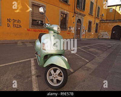 Shiny moderni scooter Vespa contrasta con coperto di graffiti storici edifici color ocra con persiane e griglie sopra le finestre del piano terra a Pisa, Italia Foto Stock