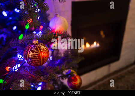 Close-up di lampadine appeso a un albero di natale con un camino in background. Foto Stock