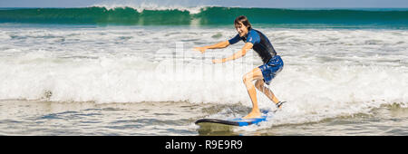 Il giovane principiante Surfer impara a navigare su una schiuma di mare sull'isola di Bali banner, formato lungo Foto Stock