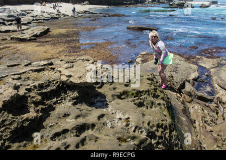 Femmina bionda esplora il robusto, spiaggia rocciosa di La Jolla California durante la bassa marea Foto Stock