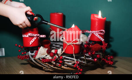 Le mani della madre e del bambino, tenendo in mano un accendino, accendendo candele sulle moderne ghirlanda di Natale con quattro candele rosse su una superficie di legno con verde Foto Stock