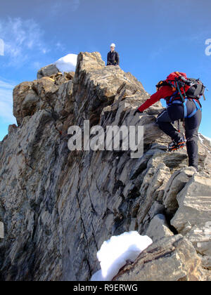Donna e uomo alpinista sul modo per un elevato picco di montagna lungo una stretta cresta rocciosa Foto Stock