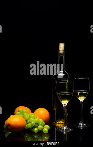 Tre Bicchieri per il vino, un grappolo di uva e arance su uno sfondo nero, studio luce Foto Stock