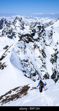 Un maschio di backcountry rider arrampicate ed escursioni a lungo esposto stretta cresta di neve nelle Alpi della Svizzera sul suo modo di un elevato picco di montagna nel Silvre Foto Stock