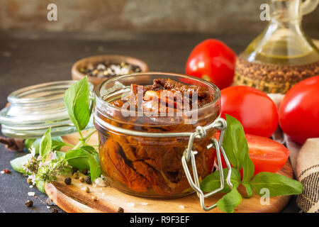 Pomodori secchi con olio di oliva in un recipiente su pietra nera o calcestruzzo tabella. Copia dello spazio. Foto Stock