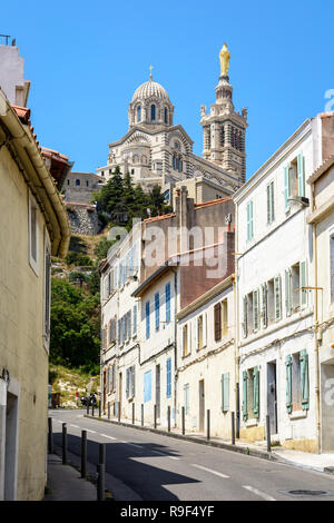 Una stretta strada in pendenza confina con vecchie case a schiera a Marsiglia, Francia, andando fino a Notre Dame de la Garde basilica sulla sommità della collina. Foto Stock