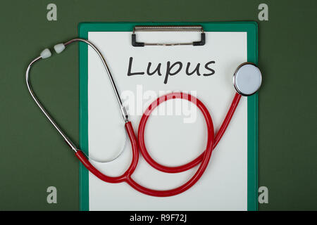 Medico workplace con appunti e il testo "Lupus', medicina stetoscopio rosso sul libro verde sullo sfondo. Prescrizione medica. Cura di salute o di malattia Foto Stock