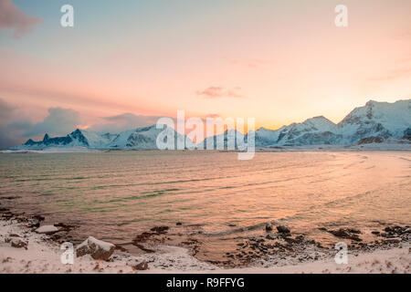 L'inverno. Fiordo norvegese circondato da montagne innevate al mattino presto. Cielo rosa dal sorgere del sole riflessa nell'acqua Foto Stock
