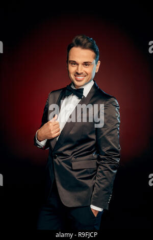 Professional showman indossare tuta in piedi isolato su nero e sfondo rosso in posa per fotocamera a sorridere allegro Foto Stock