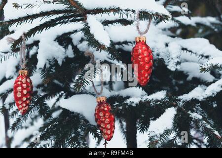 Bella giocattoli di Natale in forma di coni di abete impiccato decorare l'albero di Natale. Sui rami di abete rosso si trova buly e la neve fredda. Foto Stock