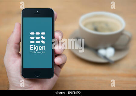 Un uomo guarda al suo iPhone che visualizza le tecnologie Eigen logo (solo uso editoriale). Foto Stock