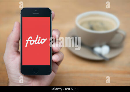 Un uomo guarda al suo iPhone che visualizza il logo di Folio (solo uso editoriale). Foto Stock