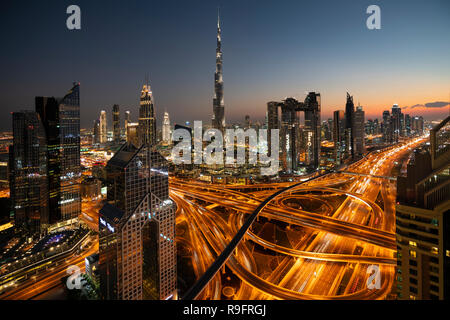 Paesaggio urbano in vista di Burj Khalifa e complesso interscambio autostradale e grattacieli lungo la Sheikh Zayed road in serata a Dubai, Emirati Arabi Uniti, Foto Stock