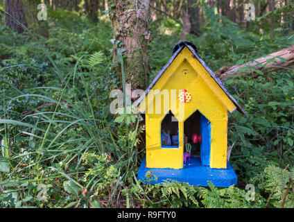 Giallo casa di fata lungo un percorso sulla costa dell'Irlanda. Casa è giallo con porta blu in una verde e lussureggiante foresta. Foto Stock