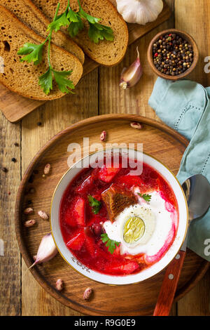 Tradizionale Russo Ucraino borscht. Borsch, zuppa di barbabietole con panna acida in un recipiente da cucina tavolo in legno. Vista superiore piatta sullo sfondo dei laici. Foto Stock
