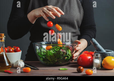 Lo Chef riversa i pomodori ciliegia in una ciotola. Gelo in movimento. Per la preparazione di insalate. E delizioso cibo sano concetto, cottura. Su sfondo grigio. Foto Stock