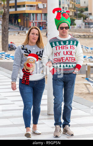 Benidorm, Costa Blanca, Spagna, 25 dicembre 2018. Turisti britannici abito per l'occasione il giorno di Natale in questo preferito getaway destinazione per gli inglesi sfuggire il freddo a casa. Temperature saranno in media-alta 20's Celsius oggi in questo hotspot del mediterraneo. Giovane uomo e donna che indossa il Natale ponticelli passeggiando onn la passeggiata fronte mare. Foto Stock
