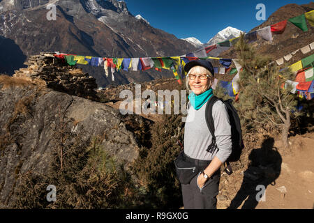 Il Nepal, Namche Bazar, femmina senior trekker appoggiato accanto a bandiere di preghiera flyng da ruvida rocky chorten, Foto Stock