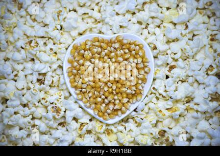 Chicchi di mais nel recipiente di forma del cuore con pronto il popcorn intorno ad esso. Foto Stock