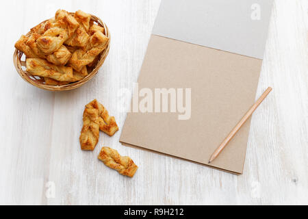 Treccia di cookie. Pasta sfoglia con cannella vicino a notebook per ricette e matita bianca su un tavolo di legno. Copyspace. Foto Stock