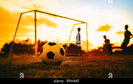 Azione Silhouette sport all aperto di un gruppo di bambini di divertirsi giocando a calcio in erba verde campo per esercizio. Foto Stock