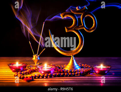 Om simbolo, incenso, fumo di candela e japa mala sul tavolo di legno a sfondo nero Foto Stock