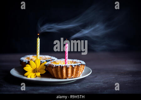 Due cheesecake con candele e con fiore giallo su sfondo nero Foto Stock