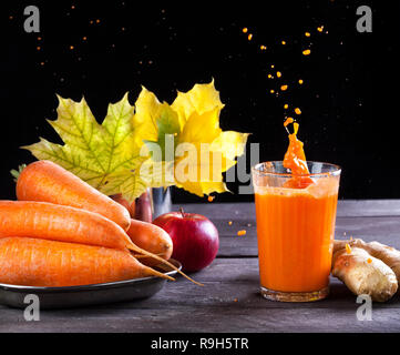 Carote fresche, Apple, succo di zenzero con spruzzi su sfondo di legno nella stagione autunnale Foto Stock