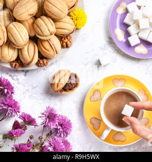 Donna mettendo mano zucchero nella tazza di caffè nei pressi di dolci fatti in casa i dadi su marmo bianco sullo sfondo Foto Stock
