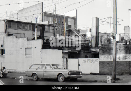 Lithgow, Australia 1977: Una vista laterale della parte posteriore degli uffici e dei negozi che mostra un disordine di costruzione confuso. In primo piano, un uomo si accovaglia vicino alla grondaia e una station wagon Ford Falcon XR è parcheggiata direttamente di fronte a un cartello "No Parking". Foto Stock