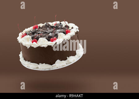 Torta al cioccolato con panna e ciliegie galleggiante sopra lo sfondo marrone con copia spazio. Foto Stock