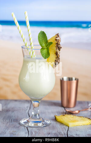 Il freddo La pina colada cocktail in un bicchiere sulla spiaggia con seascape sfondo Foto Stock