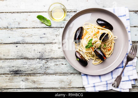 Spaghetti allo scoglio, Pasta con pesce e frutti di mare, cozze in grigio di una piastra di ceramica su sfondo di legno, vista dall'alto Foto Stock