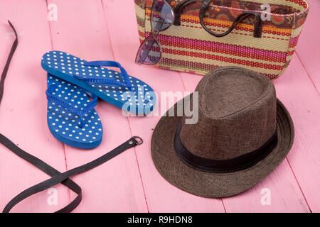 Estate accessori - Occhiali da sole, paglia borsa da spiaggia, cappello per il sole, cinghia e flip flop rosa sul tavolo di legno Foto Stock