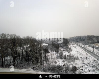 Panoramica vista aerea di una ferrovia che passa attraverso i campi innevati e foreste Foto Stock