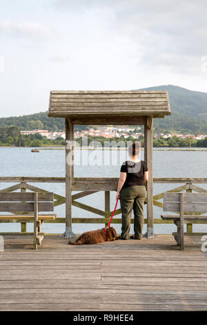 Donna sul molo sul fiume a piedi, Noia, Galizia, Spagna marrone con acqua spagnolo cucciolo di cane Foto Stock