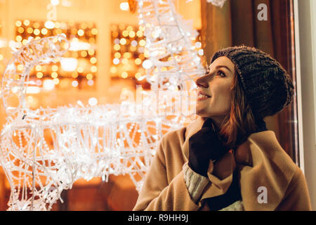 Giovane donna a piedi in città e guardando decorate vetrine di Natale di notte. Anno nuovo concetto Foto Stock