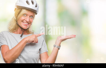La mezza età caucasian ciclista donna che indossa il casco di sicurezza su sfondo isolato stupiti e sorridente alla fotocamera durante la presentazione con la mano e puntare Foto Stock
