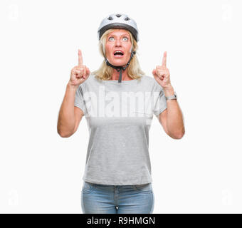 La mezza età caucasian ciclista donna che indossa il casco di sicurezza su sfondo isolato meravigliato e sorpreso cercando e dispositivo di puntamento con le dita e sollevato Foto Stock
