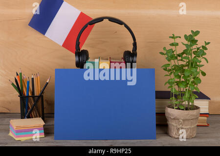 Concetto di apprendimento della lingua francese - carta bianca, bandiera della Francia, libri, cuffie, matite su sfondo di legno Foto Stock