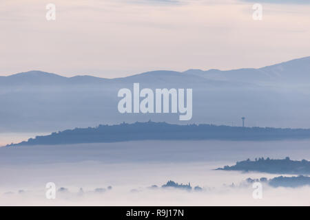 La nebbia di riempimento di una valle in Umbria (Italia), con strati di montagne e colline e varie sfumature di blu Foto Stock