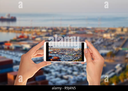 Un turista è scattare una foto del terminale della porta con contenitori, nuove vetture e vagoni nelle prime ore del mattino su un telefono cellulare Foto Stock