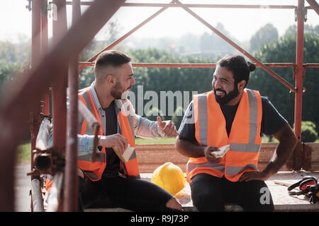 Le persone che lavorano nel sito in costruzione. Gli uomini al lavoro nel nuovo progetto di alloggiamento. Team di lavoratori felice ridendo e parlando e mangiando snack durante la pausa pranzo Foto Stock