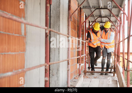 Le persone che lavorano nel sito in costruzione. Giovani uomini al lavoro in casa nuova all'interno di un condominio. Latino lavoratore manuale aiutando feriti co-lavoratore dopo ac Foto Stock