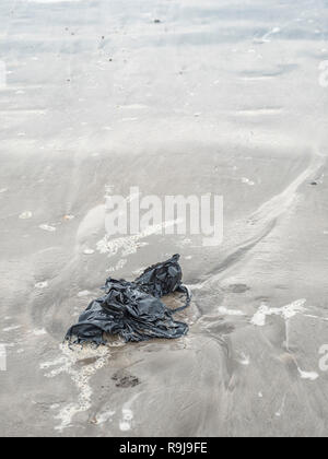 Plastica nero bin liner lavato fino a riva & costiera di inquinanti. Metafora plastica inquinamento, inquinamento ambientale, guerra di plastica Rifiuti in plastica Foto Stock