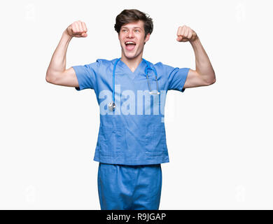 Giovane medico medico che indossano uniformi su sfondo isolato che mostra i muscoli di armi sorridente fieri. Concetto di fitness. Foto Stock